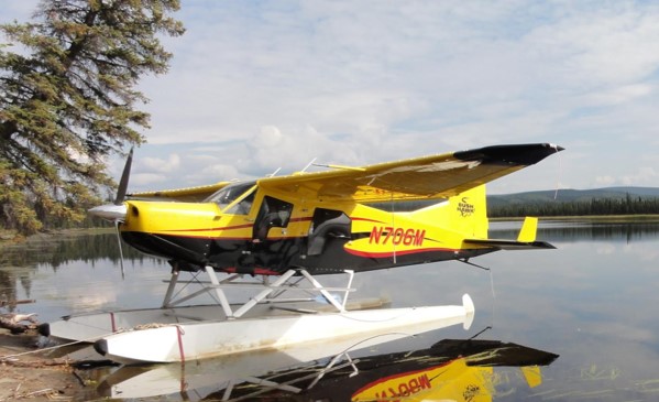 propeller plane with water skids sitting next to the shore of a lake