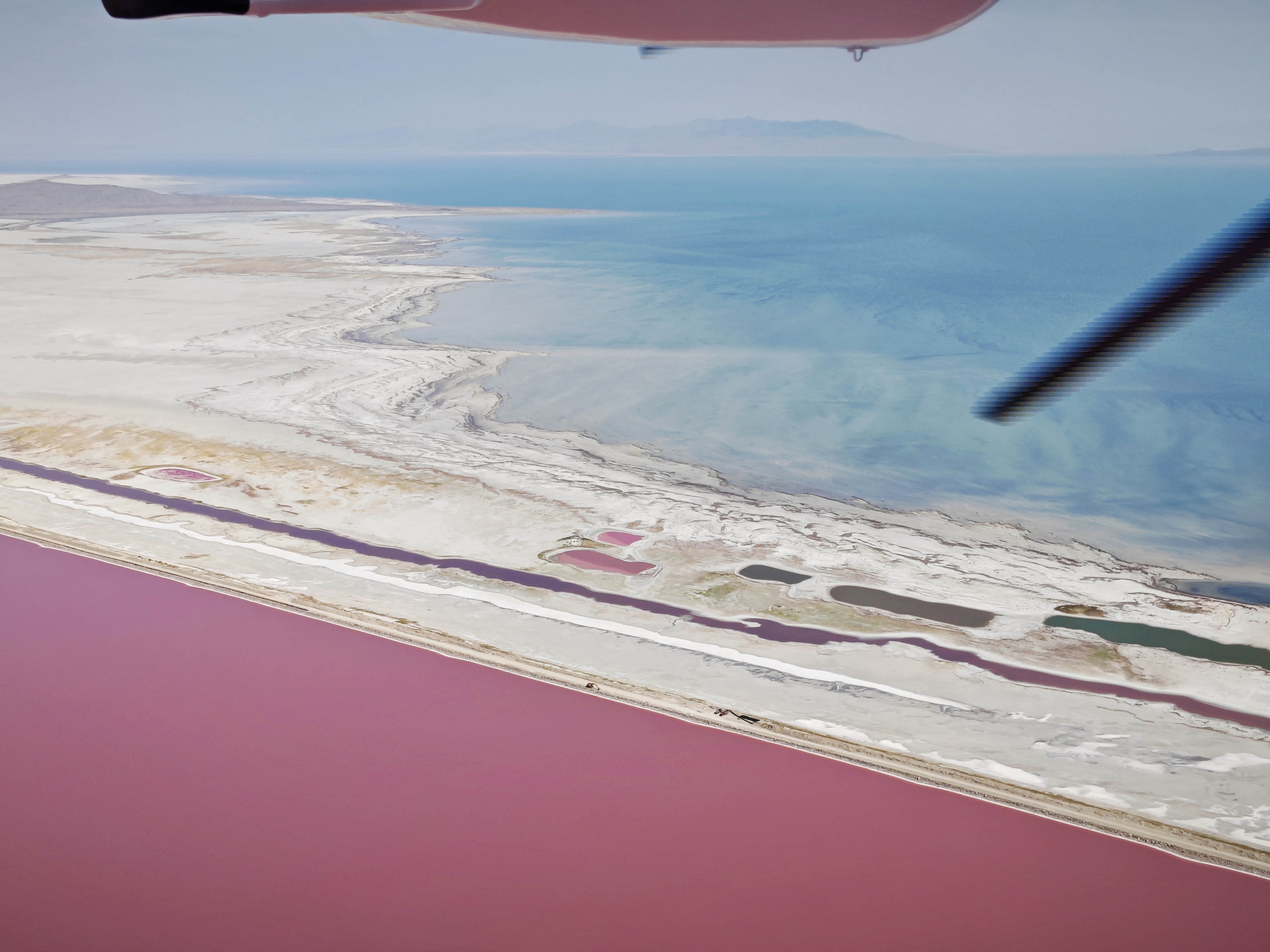 photo of a pink lake in the foreground, white sand and blue lake in the background. Taken from a propeller plane