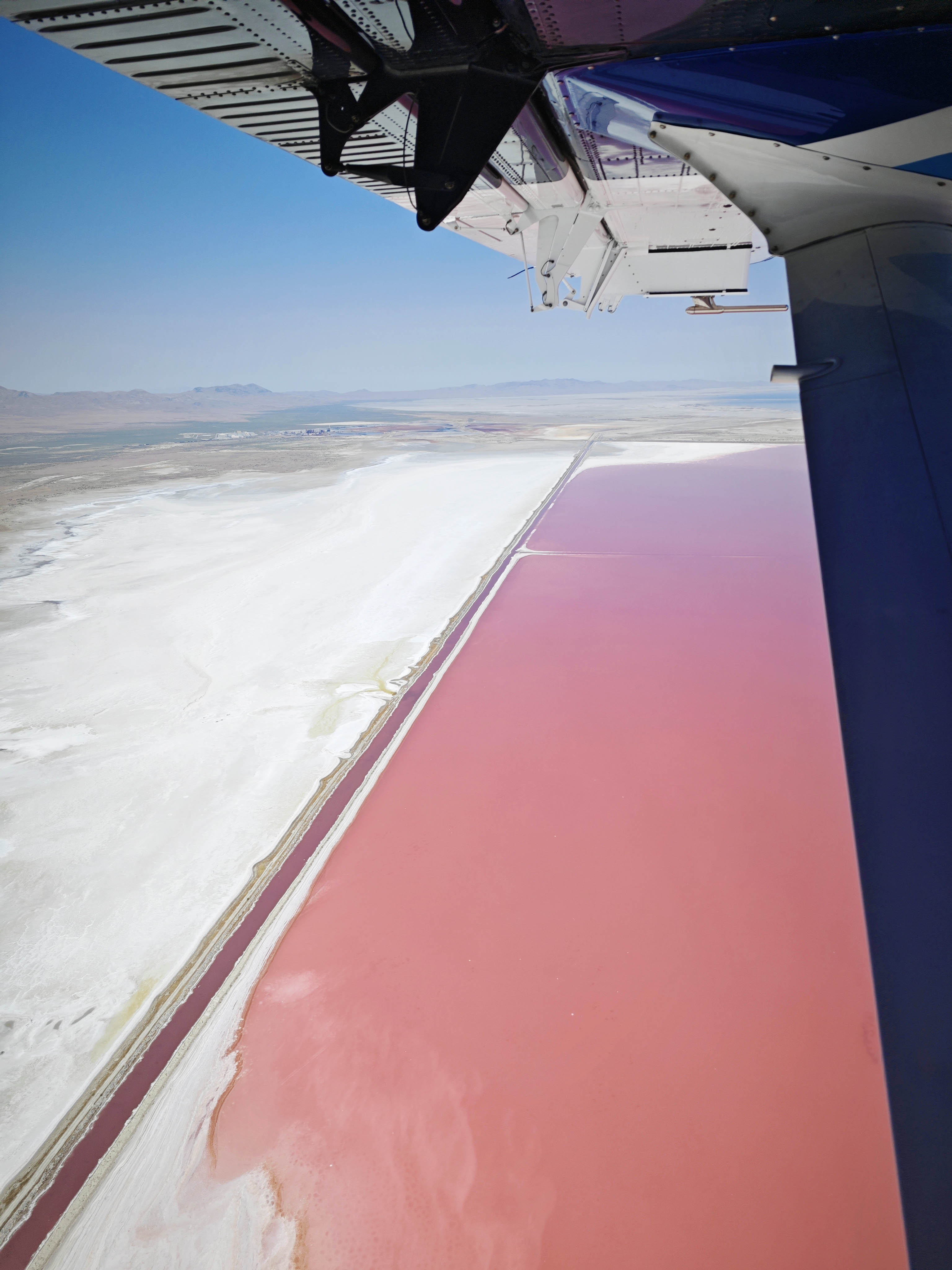 photo of pink lake and white sand shoreline from the window of a plane