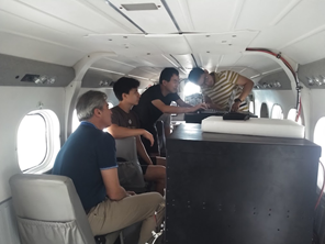 Four men sitting in the cabin of a small plane, making adjustments to instruments