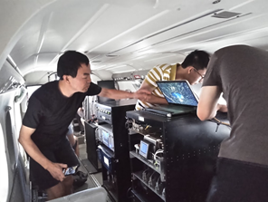 three mean working on a computer rack inside the cabin of a small plane